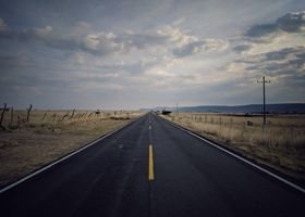 Discover the beauty of an empty desert highway leading into the horizon under a vibrant sunset sky.