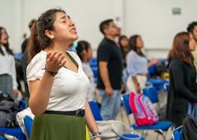 Young adults engaged in a worship celebration indoors, raising hands in prayer.