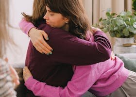 Side view of positive friends sitting and embracing each other during session with unrecognizable psychologist in light room